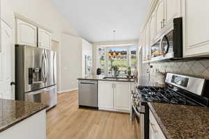 Kitchen with appliances with stainless steel finishes, a peninsula, light wood-style floors, decorative backsplash, and lofted ceiling