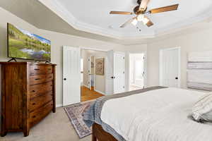 Bedroom featuring ornamental molding, a raised ceiling, light colored carpet, connected bathroom, and ceiling fan