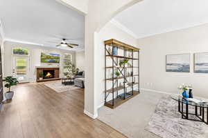 Sitting room with crown molding, a ceiling fan, arched walkways, a brick fireplace, and wood finished floors