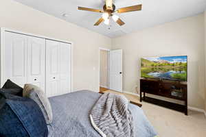 Bedroom with light colored carpet, a closet, and ceiling fan