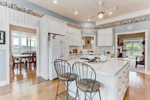 Kitchen with white appliances, a center island, light countertops, ceiling fan, and a kitchen breakfast bar