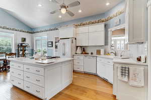 Kitchen featuring white appliances, a ceiling fan, vaulted ceiling, plenty of natural light, and light countertops