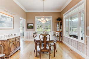 Dining room with a chandelier, wainscoting, light wood-style flooring, crown molding, and plenty of natural light