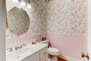 Bathroom featuring wallpapered walls, wainscoting, vanity, and wood finished floors