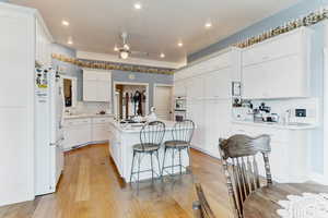 Kitchen featuring white appliances, a ceiling fan, a kitchen breakfast bar, light countertops, and light wood-type flooring