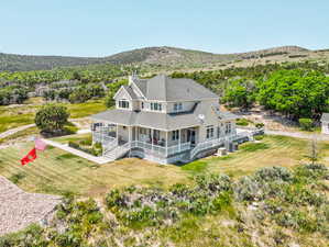 Rear view of house featuring covered porch, a chimney, roof with shingles, a mountain view, and a lawn