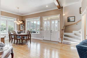 Dining space with a chandelier, stairs, light wood finished floors, beam ceiling, and ornamental molding
