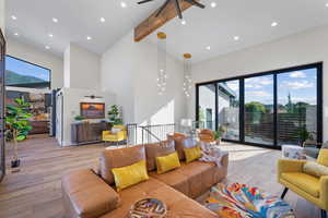 Living area with high vaulted ceiling, light wood-style flooring, a ceiling fan, healthy amount of natural light, and beam ceiling