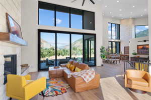 Living room featuring a towering ceiling, a glass covered fireplace, wood finished floors, recessed lighting, and a ceiling fan