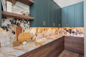 Kitchen featuring open shelves, decorative backsplash, light wood-style flooring, and light stone counters