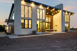 Back of property at dusk featuring an outdoor hangout area, a chimney, a balcony, and stone siding