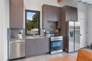 Kitchen featuring appliances with stainless steel finishes, tasteful backsplash, light stone countertops, and gray cabinets