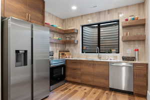 Kitchen featuring appliances with stainless steel finishes, open shelves, brown cabinets, light wood finished floors, and decorative backsplash