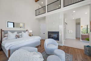 Bedroom featuring a towering ceiling, wood finished floors, a fireplace, and recessed lighting. You can see the railing above where the loft is