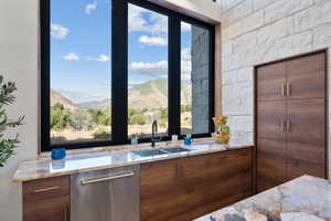 Kitchen featuring stainless steel dishwasher, light stone counters, and healthy amount of natural light