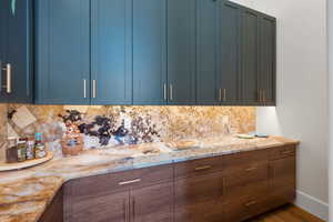 Kitchen with blue cabinetry, tasteful backsplash, light stone countertops, and wood finished floors