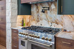 Kitchen with double oven range, backsplash, extractor fan, and light stone countertops
