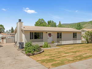 Single story home featuring a mountain view, a chimney, a shingled roof, and a front lawn