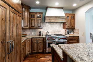 Kitchen with range with two ovens, premium range hood, dark wood finished floors, light stone counters, and arched walkways