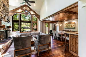 Living area featuring a stone fireplace, a chandelier, a ceiling fan, dark wood-style flooring, and high vaulted ceiling