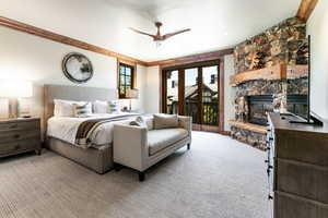 Bedroom with access to exterior, light carpet, a stone fireplace, and a ceiling fan
