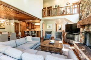 Living area with a chandelier, a stone fireplace, dark wood-style flooring, and a towering ceiling