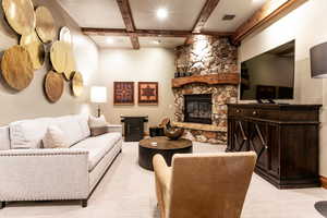 Living room featuring light colored carpet, beamed ceiling, a stone fireplace, and recessed lighting