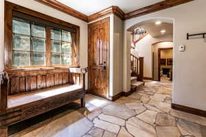 Foyer featuring stone flooring, stairs, arched walkways, and crown molding