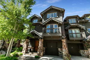 Craftsman-style home featuring a balcony, an attached garage, concrete driveway, and stone siding