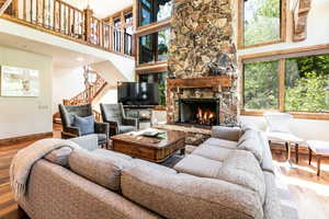 Living area featuring stairway, wood finished floors, a stone fireplace, and a high ceiling