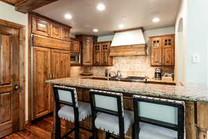 Kitchen with premium range hood, built in appliances, dark wood-type flooring, light stone counters, and a breakfast bar
