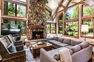 Living area with high vaulted ceiling, a stone fireplace, and wood finished floors