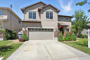 Traditional-style home featuring stucco siding, brick siding, an attached garage, and driveway