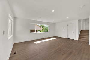 Unfurnished living room featuring dark wood finished floors, stairway, and recessed lighting