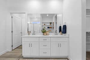 Bathroom with double vanity, a walk in closet, and wood finished floors