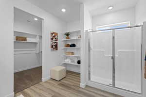 Full bath with a stall shower, a spacious closet, wood finished floors, and recessed lighting