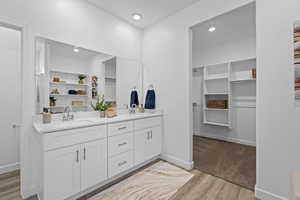 Full bath featuring double vanity, wood finished floors, a spacious closet, and recessed lighting