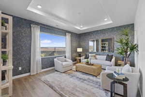 Living room with a tray ceiling, wood finished floors, recessed lighting, and wallpapered walls