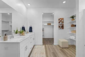 Full bath featuring double vanity, wood finished floors, a spacious closet, and recessed lighting