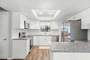 Kitchen featuring stainless steel appliances, open shelves, a tray ceiling, light wood-type flooring, and a peninsula