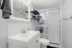 Full bathroom featuring a stall shower, backsplash, and vanity