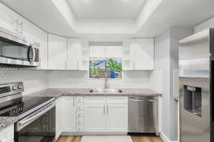 Kitchen with appliances with stainless steel finishes, open shelves, white cabinets, and light wood-style floors