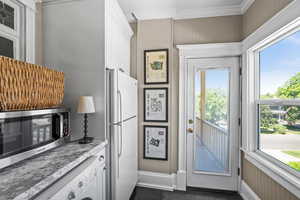 Kitchen with freestanding refrigerator, ornamental molding, washer / dryer, white cabinetry, and stainless steel microwave