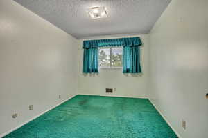 Carpeted spare room with a textured ceiling and baseboards