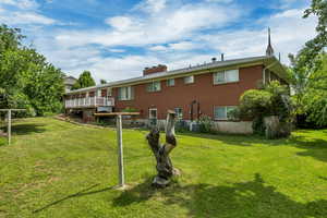Back of property with brick siding, a lawn, a wooden deck, and a chimney