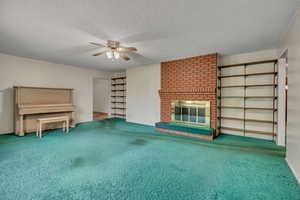 Unfurnished living room with a ceiling fan, a brick fireplace, carpet, and a textured ceiling