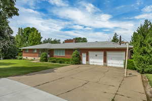 Single story home with a garage, brick siding, a front lawn, driveway, and a chimney