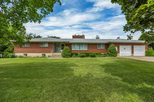 Ranch-style house featuring brick siding, an attached garage, a front lawn, and driveway