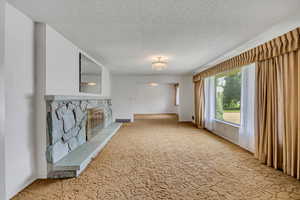 Unfurnished living room with carpet, a textured ceiling, and a stone fireplace