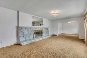Unfurnished living room featuring carpet floors, a stone fireplace, and a textured ceiling